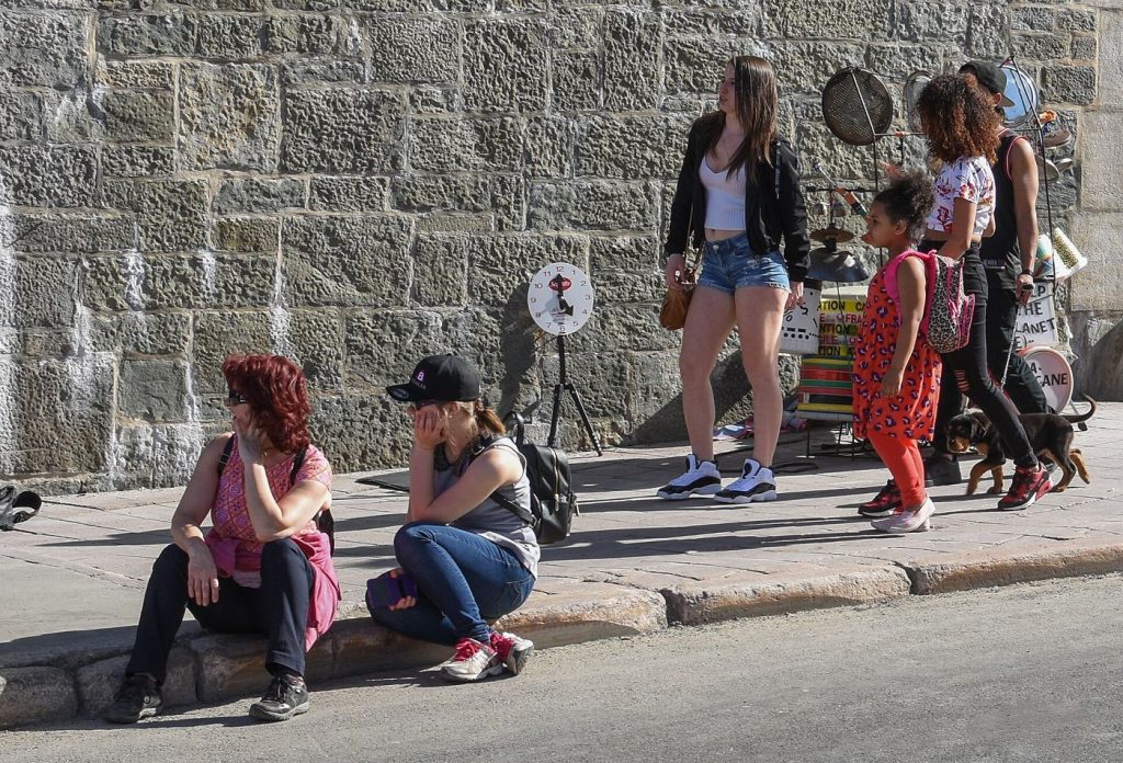 People wait in the shade at a city bus stop on a bright, hot summer afternoon.