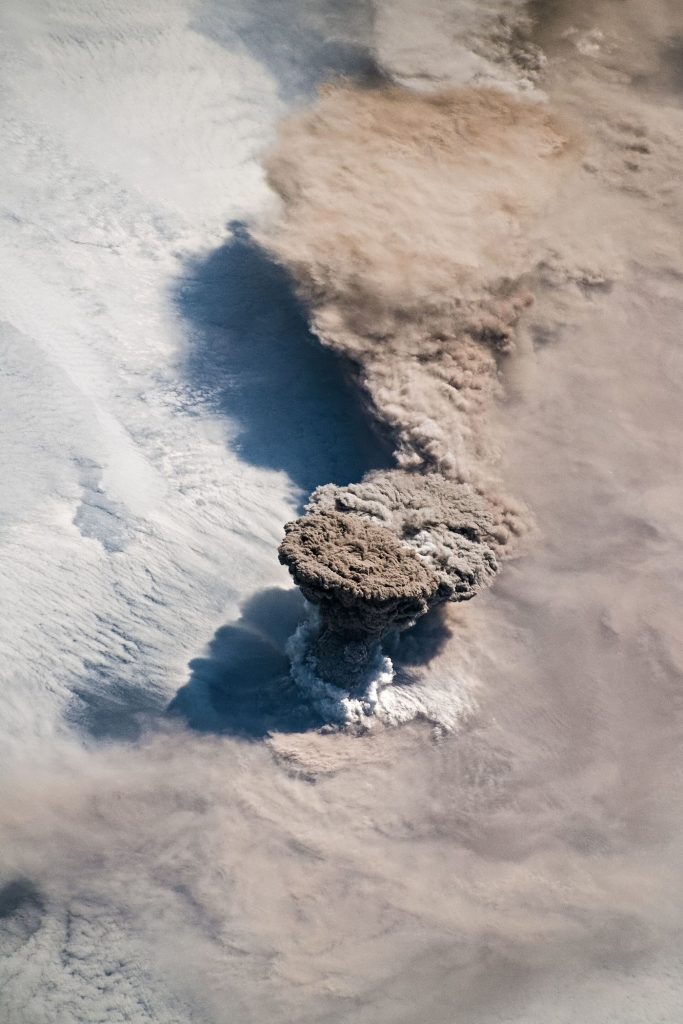 island volcano with ash cloud above dark lava fields reaching the sea